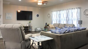 Una sala de estar con un sofá, un sillón reclinable, una mesa de centro, un televisor de pantalla plana, un ventilador de techo y adornos en las paredes.