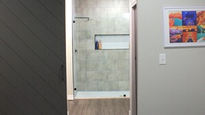 Un dormitorio con cama, puerta corredera, baño con ducha y estante fijado a la pared.