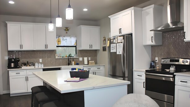 Una cocina moderna con armarios blancos, electrodomésticos de acero inoxidable e iluminación colgante.