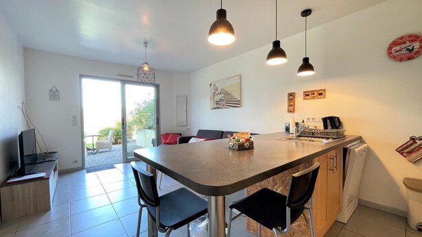 Una cocina moderna con una isla central, iluminación colgante y una zona de comedor con sillas.