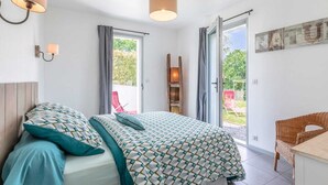 Un dormitorio con cama, dos lámparas de pared, un ventanal con cortinas, una escalera de madera y una silla de mimbre.