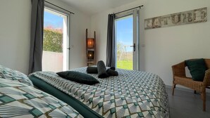 Un dormitorio con una cama grande, dos ventanas, una silla de mimbre y un aplique de pared.