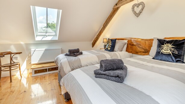 Une chambre confortable avec un plafond en pente, une grande fenêtre, une chaise en bois et un lit avec une literie à rayures et une décoration en forme de cœur.