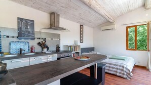 Cozinha moderna com ilha central, área de refeições com cama e janela com vista para o verde.