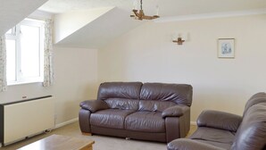 A living room with a brown leather sofa, a wooden coffee table, and a radiator. - Mariners Rest - UK44498 (Hope Cove, near Kingsbridge)