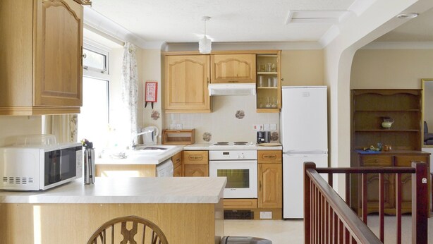 A compact kitchen with wooden cabinets, a microwave, a sink, and a stove. There's a dining table with chairs and a trash bin. - Mariners Rest - UK44498 (Hope Cove, near Kingsbridge)