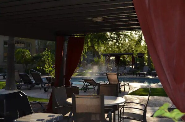 An outdoor seating area with tables and chairs, a pool, and a covered section with red curtains.