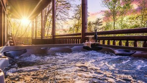Ein Whirlpool mit Holzterrasse und Geländer, umgeben von Bäumen und einem Sonnenuntergang im Hintergrund.