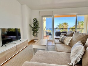 A modern living room with a flat-screen TV, a sofa, a coffee table, and a potted plant.