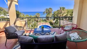 A balcony with a view of the sea, outdoor furniture, and a pool.