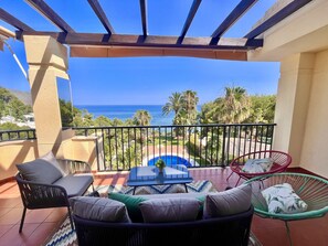 A balcony with a view of the sea, outdoor furniture, and a pool.