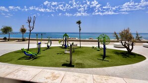 A circular outdoor area with exercise equipment, a paved walkway, and a view of the sea.