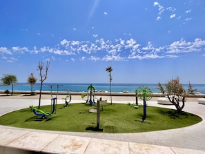 A circular outdoor area with exercise equipment, a paved walkway, and a view of the sea.