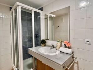 Ein Badezimmer mit einer Glaskabine zur Dusche, einem Waschbecken, einem Spiegel und einem Handtuchhalter.