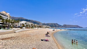 A beach with pebbles, a few umbrellas, and people.