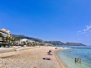 A beach with pebbles, a few umbrellas, and people.