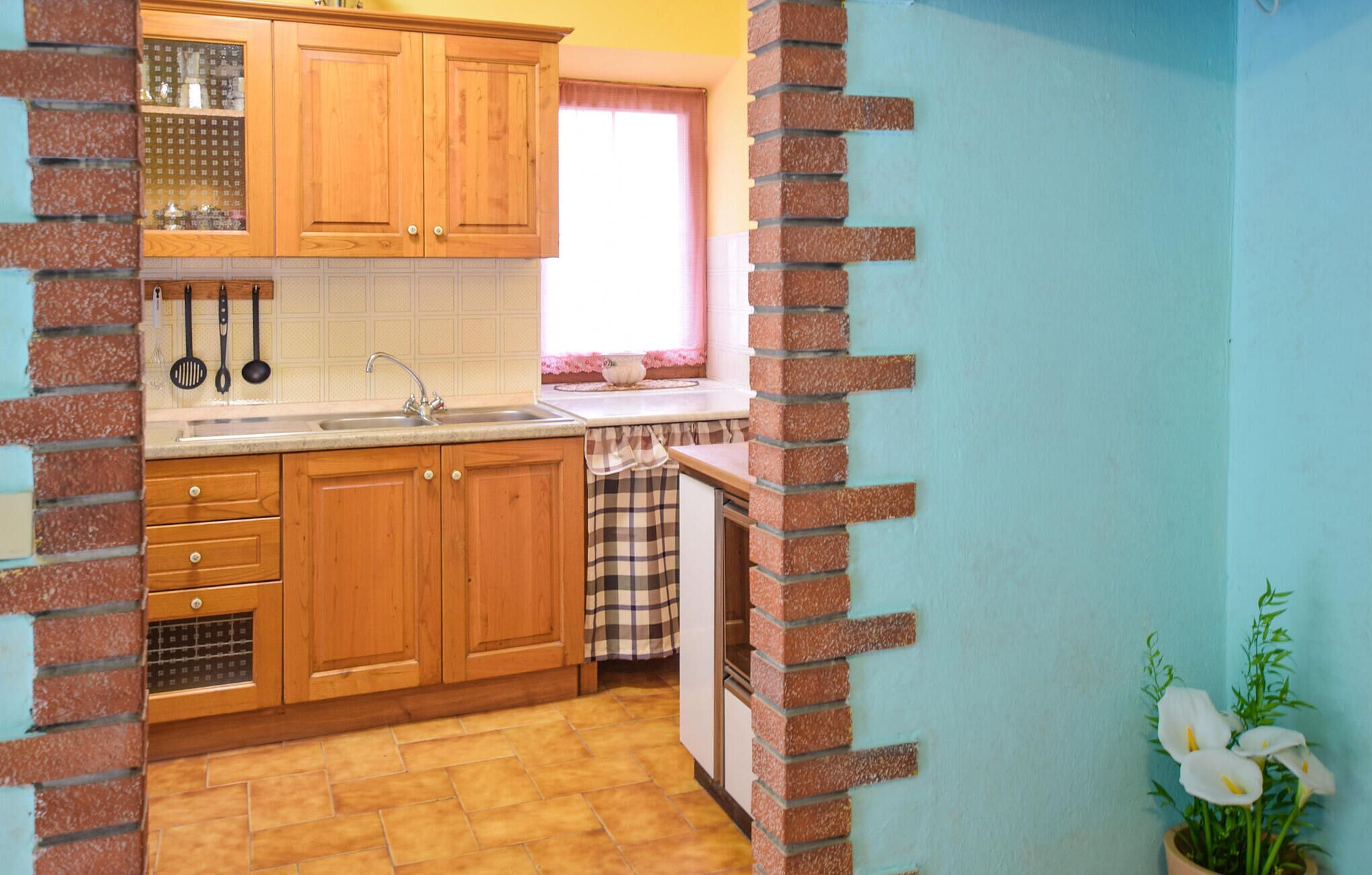 A kitchen with wooden cabinets, a sink, and a window with a pink curtain.