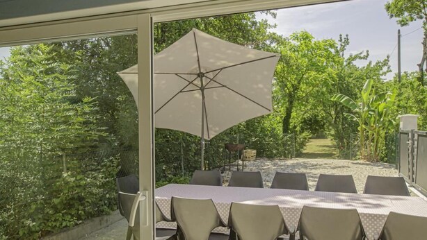 An outdoor dining area with a table and chairs, a large umbrella, and a view of a garden. - Le Gîte des Remparts (CHAOURCE)