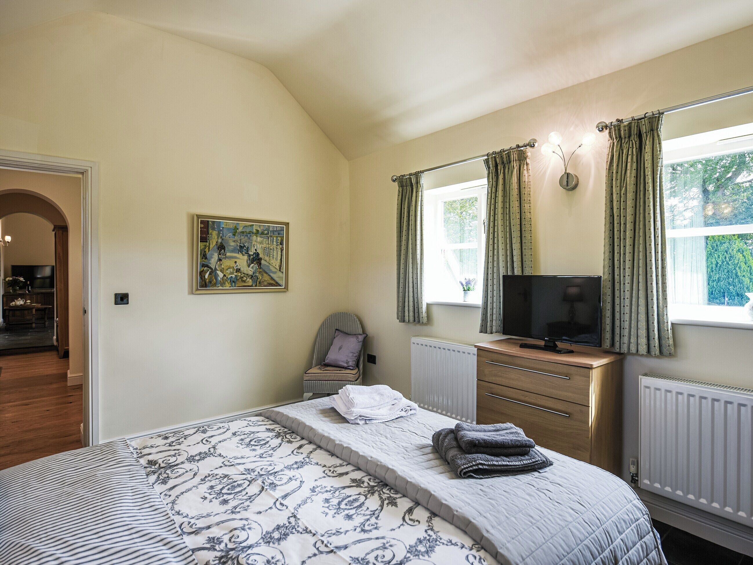 A bedroom with a bed, a television, a chair, a painting, and a window with curtains.