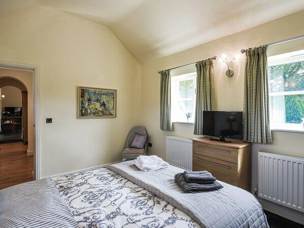A bedroom with a bed, a television, a chair, a painting, and a window with curtains.