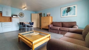 A living room with a brown sofa, a wooden coffee table, and a dining area with a table and chairs. - Cozy apartment in Oostende with WiFi (Oostende)