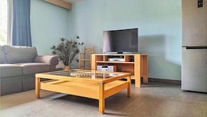 A living room with a sofa, a glass coffee table, a TV on a wooden stand, and a refrigerator. - Cozy apartment in Oostende with WiFi (Oostende)