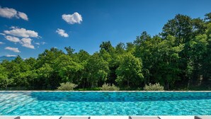 Piscina com água azul cristalina, rodeada por árvores verdes exuberantes e um deck de madeira com espreguiçadeiras.