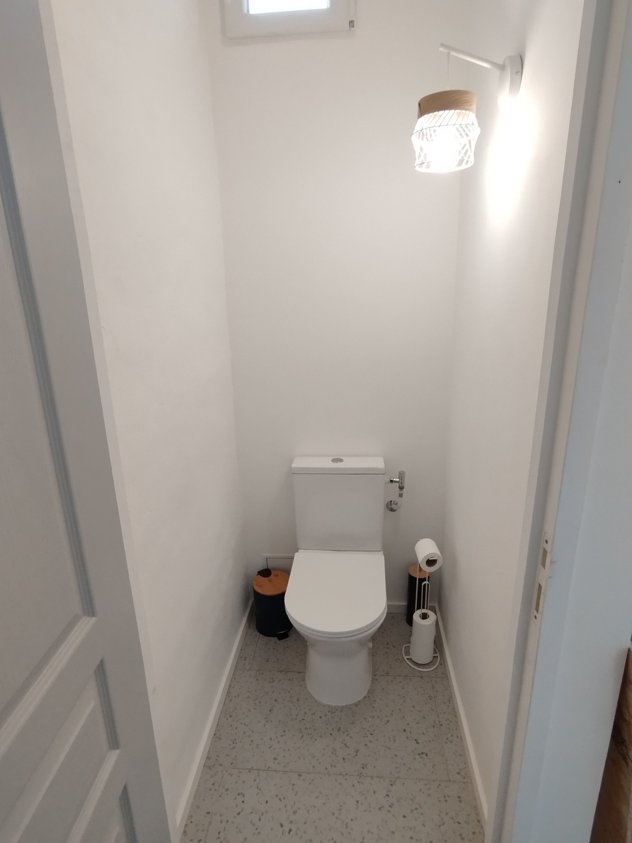 A small, narrow bathroom with a white toilet, a trash bin, and a toilet paper holder.