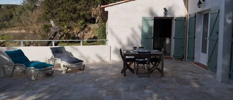 Um pátio externo com mesa, cadeiras e uma poltrona de descanso, além de uma porta com portões.