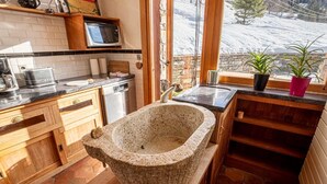Eine Küche mit Spüle aus Stein, Holzschränken, einer Mikrowelle und Blick auf eine verschneite Landschaft.