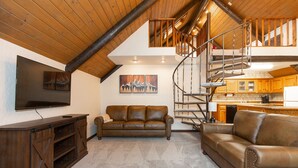 A spacious living area with a large brown leather sofa, a wooden entertainment unit, and a staircase leading to an upper level. - Cozy Hyalite Cabin! Minutes from MSU, Downtown Bozeman & Hyalite Canyon! (Bozeman)