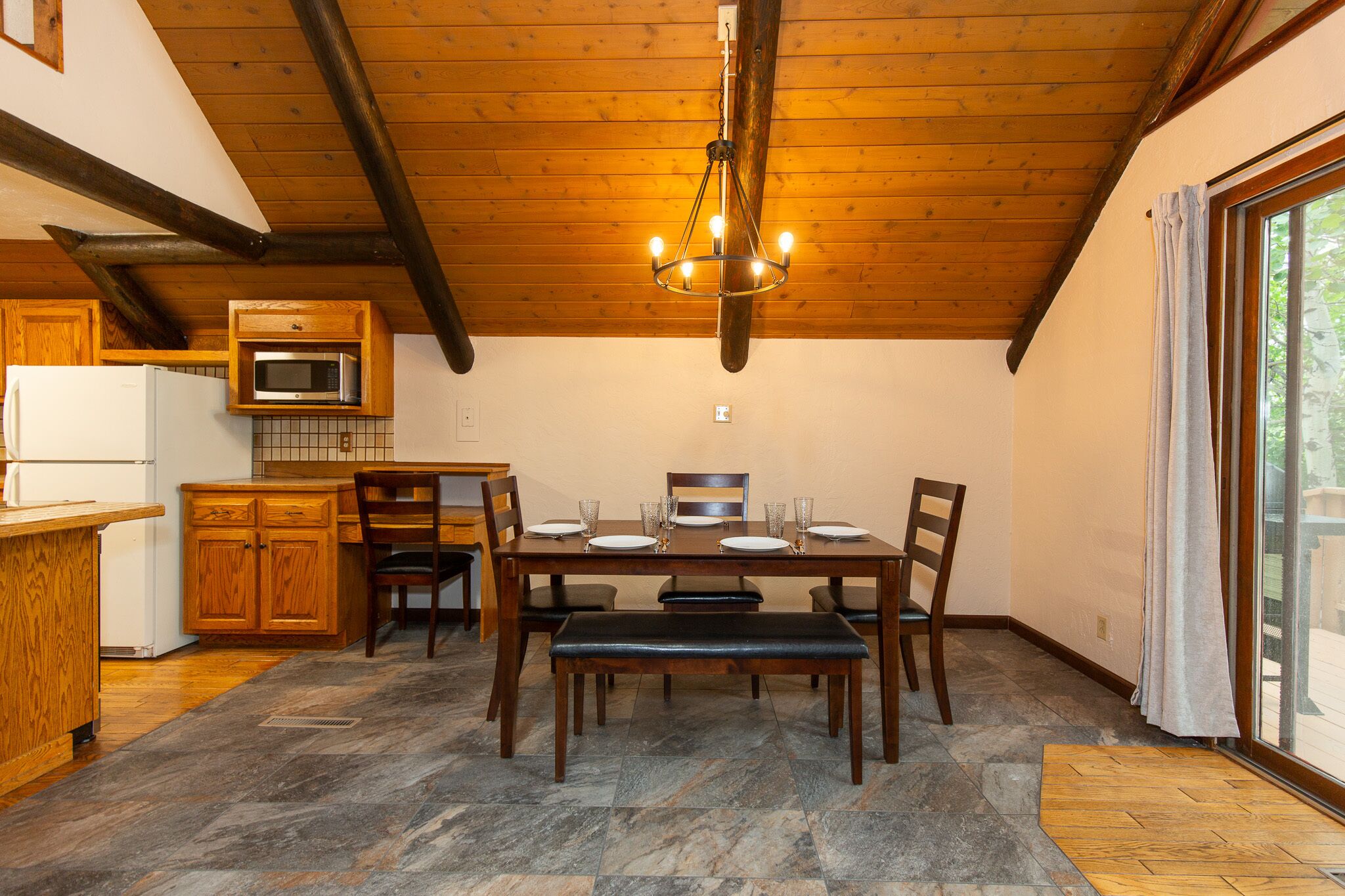 A dining area with a wooden table set for four, a bench, and a chandelier.