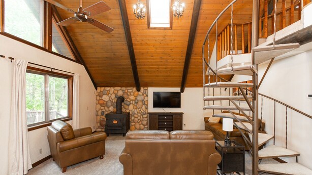 A cozy living room with a fireplace, a sofa, a TV, and a spiral staircase. - Cozy Hyalite Cabin! Minutes from MSU, Downtown Bozeman & Hyalite Canyon! (Bozeman)