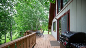 A wooden deck with a grill and outdoor furniture, surrounded by trees. - Cozy Hyalite Cabin! Minutes from MSU, Downtown Bozeman & Hyalite Canyon! (Bozeman)