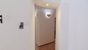 Een smalle gang met een witte muur, een kleine stoel en een ingebouwde plafondlamp.
