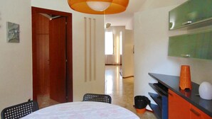 Een kamer met een eettafel, stoelen, een hangende oranje hanglamp, een spiegel en een kitchenette.