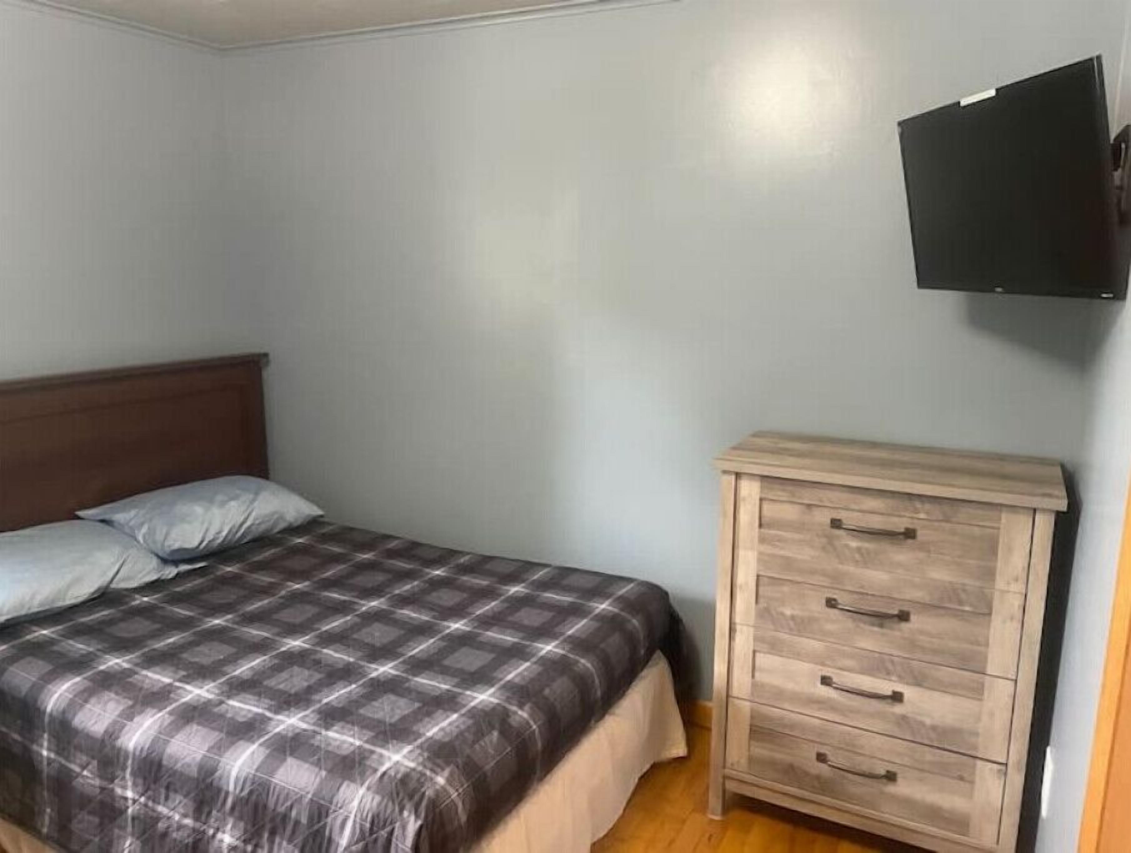 A bedroom with a bed, a wooden dresser, and a mounted TV.