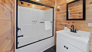 Ein modernes Badezimmer mit einer gläsernen Dusche, einem weißen Waschtisch und einer Holzbalkendecke.