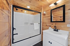 Bathroom features a frameless glass shower enclosure, a white sink, and a cabinet with two drawers.