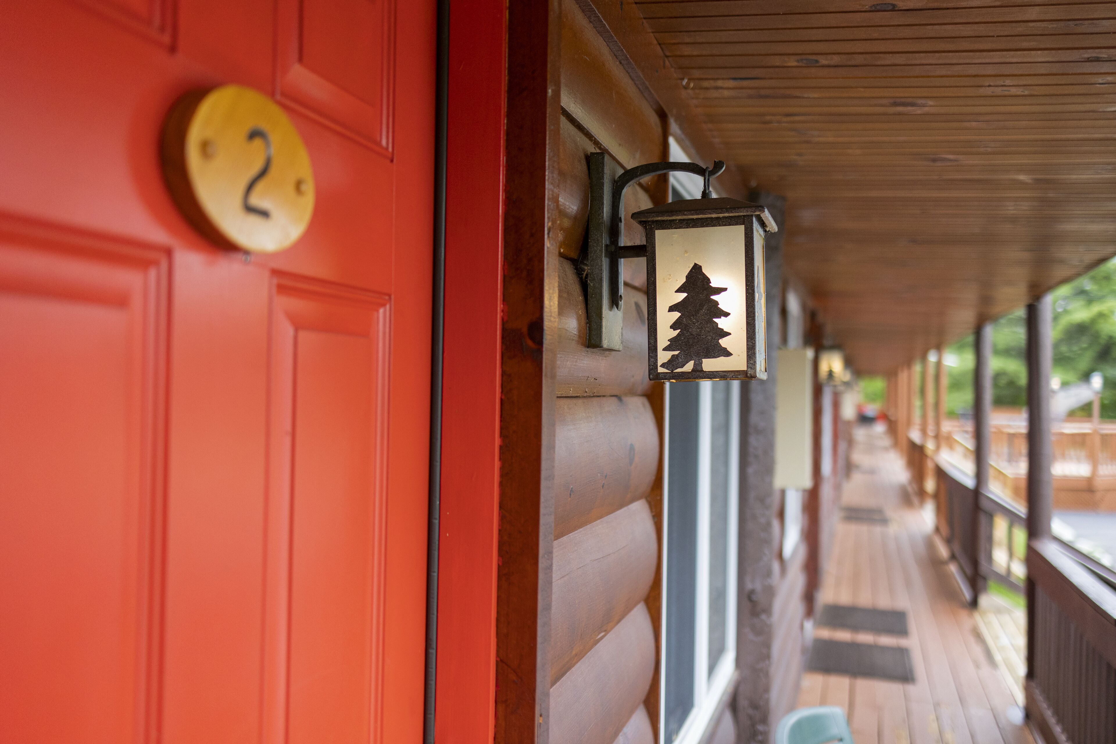 A red door with a number plate, a lantern with a tree silhouette, and a wooden porch with a railing.