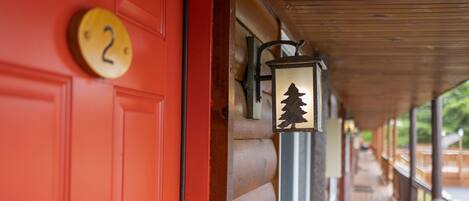 A red door with a number plate, a lantern with a tree silhouette, and a wooden porch with a railing.