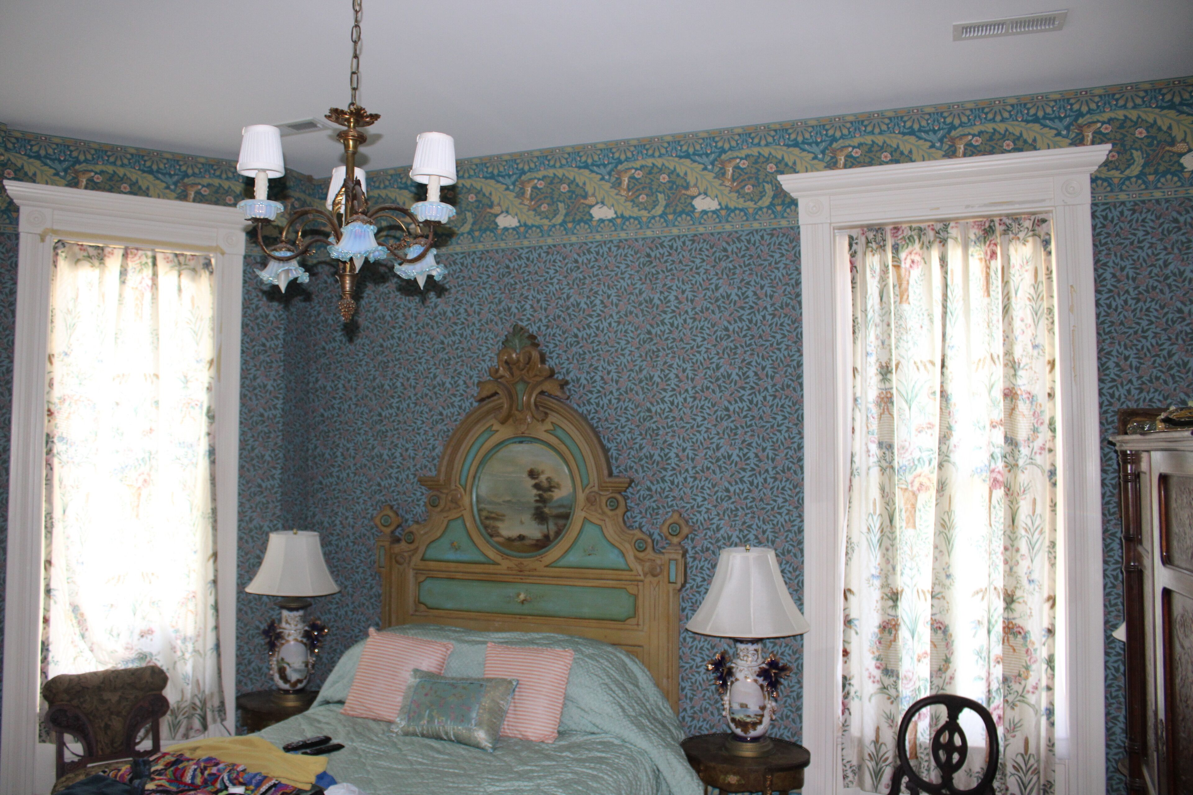 A bedroom with a bed, two nightstands, a chair, and a chandelier.