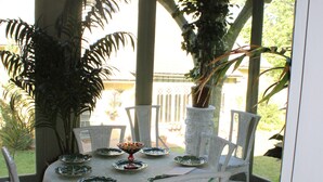 A covered outdoor dining area with a round table, white wicker chairs, and potted plants. - Johnstone Mansion (Keokuk)