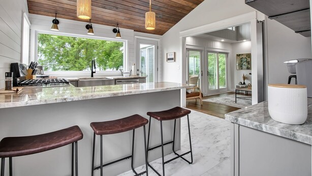 Una cocina moderna con una isla grande, taburetes de bar, iluminación colgante y vistas al exterior.