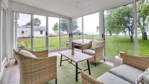 Un solárium con mobiliario de mimbre, ventanas amplias y vista a un jardín con césped.