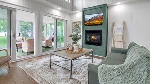 Una sala de estar moderna con chimenea, un sofá, una mesa de centro y vistas al exterior a través de puertas corredizas de vidrio.
