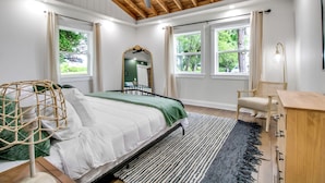 Un dormitorio con cama, escritorio, silla, ventilador de techo y ventanas con cortinas.