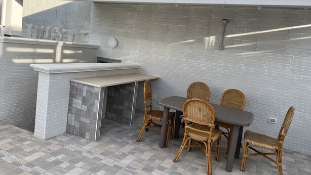 Een terras buiten met een stenen open haard, rieten stoelen en een tafel.