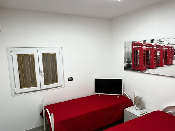 A room with two beds, a window, a wall-mounted TV, a lamp, and a poster of red telephone booths.
