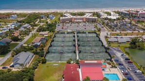 Vista aérea de un hotel costero con varias canchas de tenis, piscina y vistas a la playa.